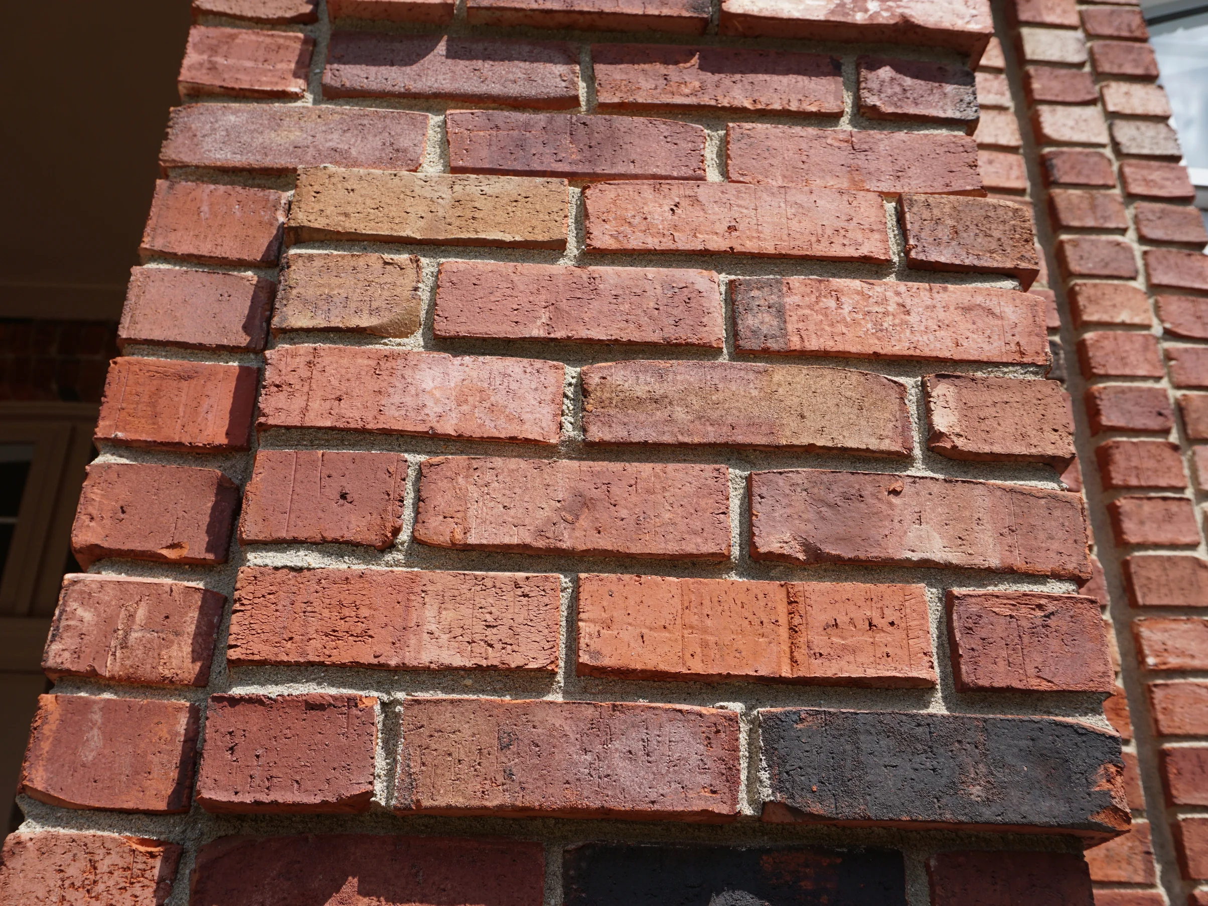 Close view of an outside brick corner of the house in 2019, the units in reds, buffs and near-blacks with pale mortar joints
