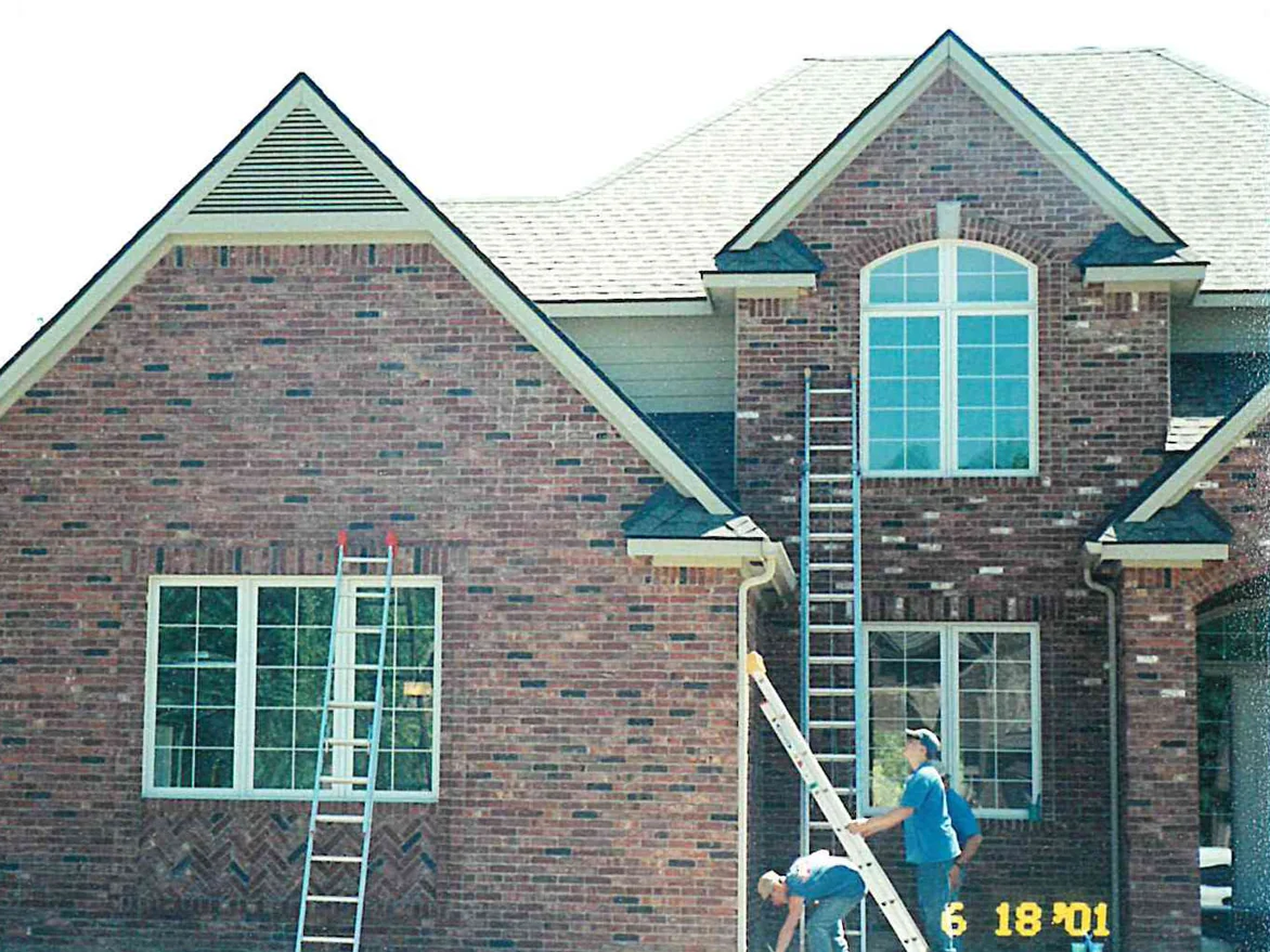 Two applicators working from ladders across the front of a two-story brick house in 2001, bright white units scattered through the wall