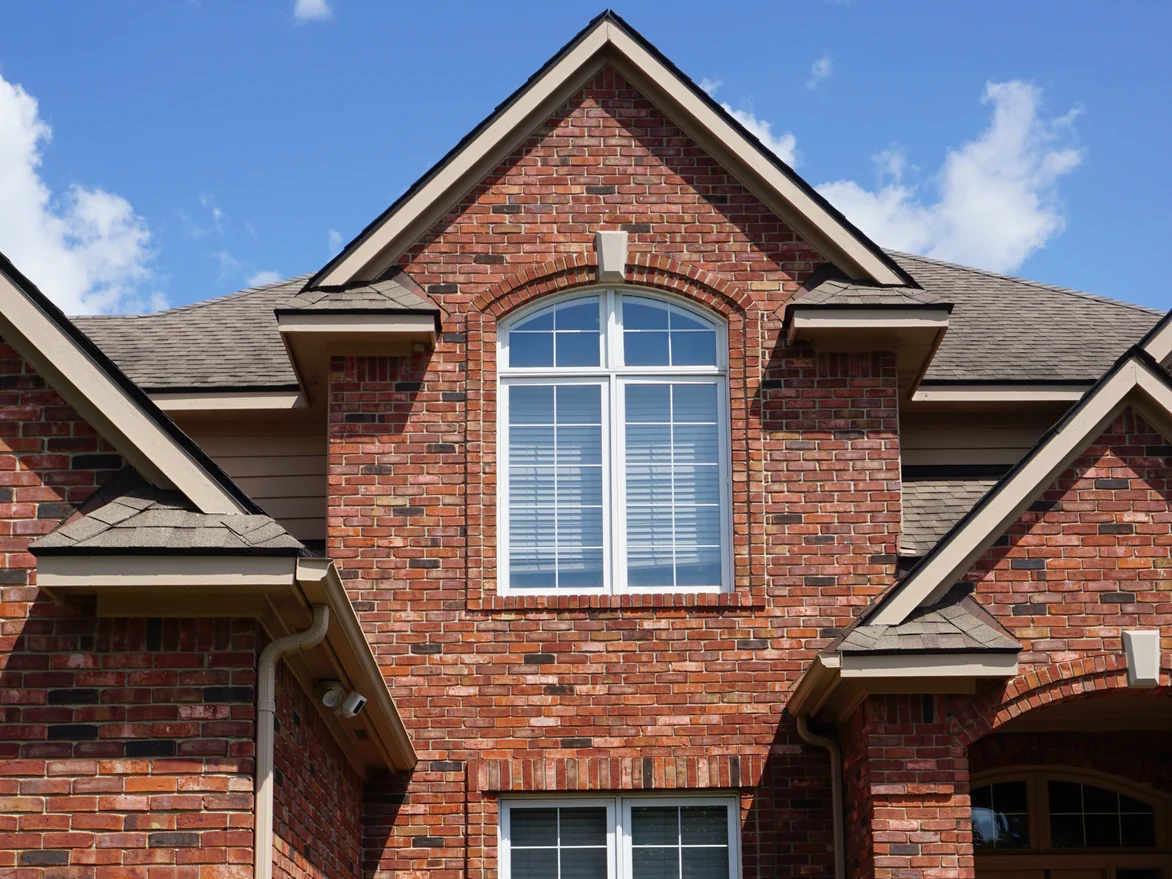 The two-story gable of the house in 2019, an arched window set in brick that reads as one range of reds, browns and buffs