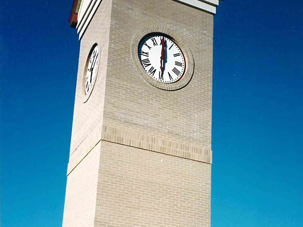 A brick clocktower during the 1994 work, the shaft under its two clock faces blotched with pale and grey patches