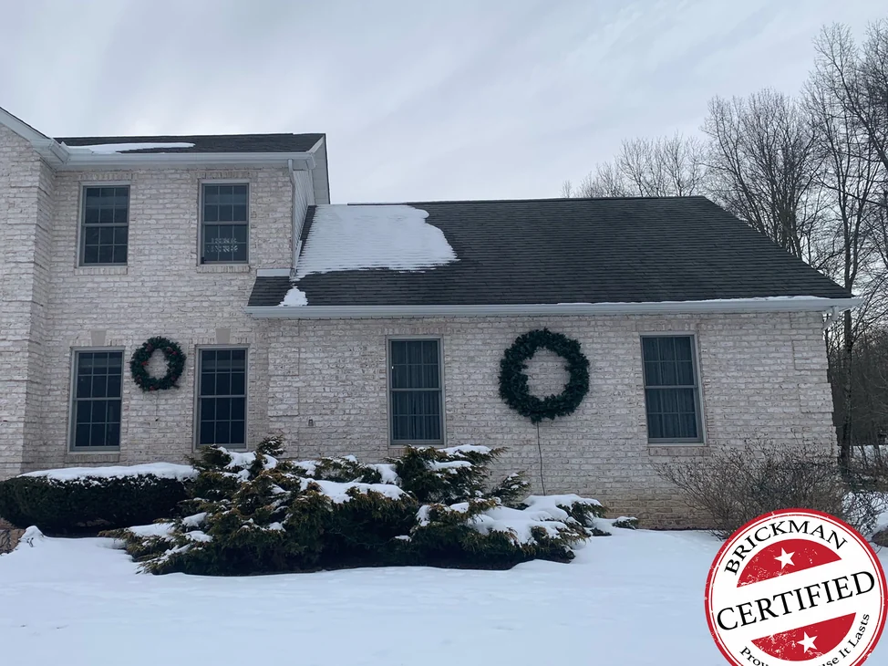 The front of the Brookfield home in winter 2021, white tumbled brick across the two-story block and the one-story wing, wreaths on the windows and snow on the roof