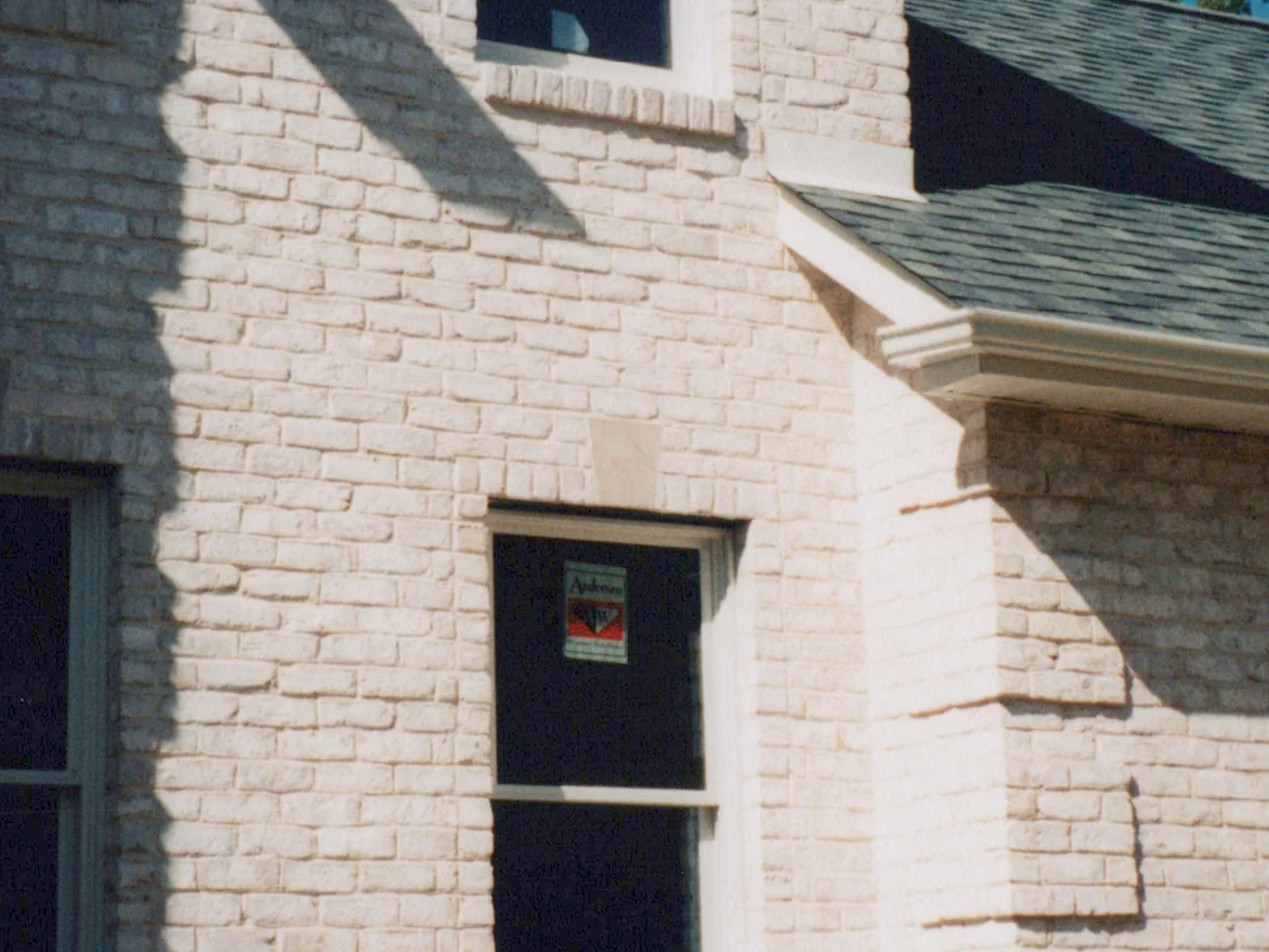 The same front wall and the corner of the one-story wing in 1998 after staining, the tumbled brick one white range in low sun with the sticker still on the window