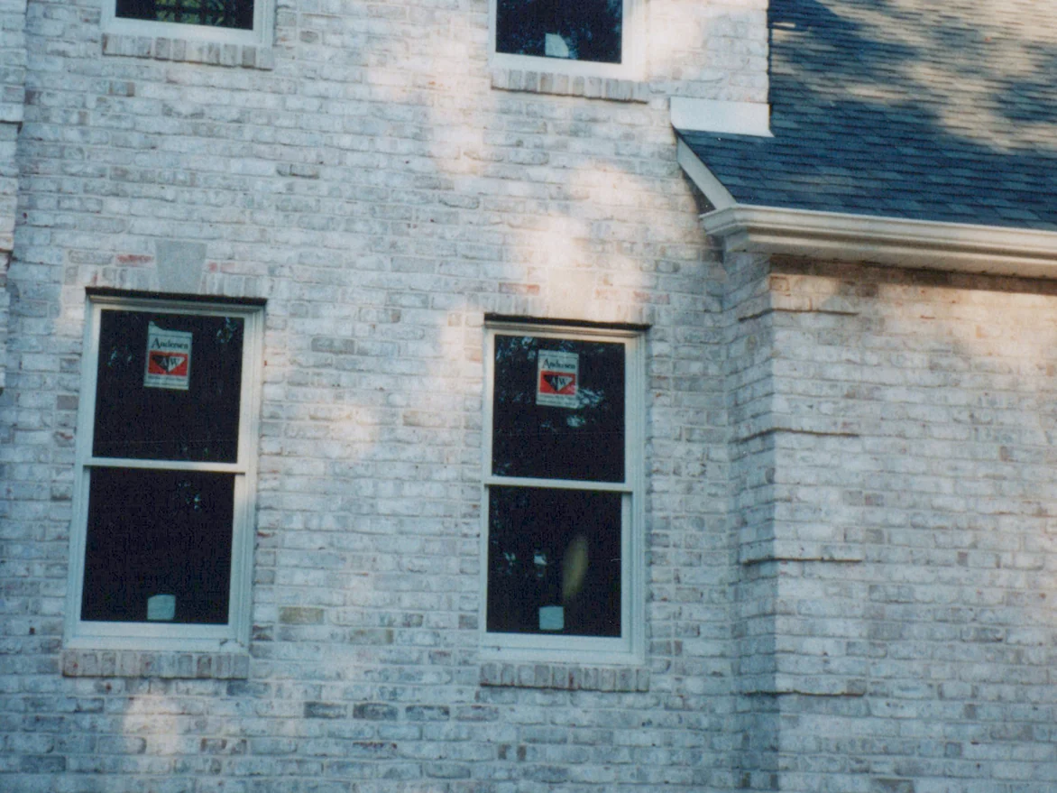 Two ground-floor windows on the front of the house in 1998, the pale tumbled brick around them marked with pink and red smudges, window maker's stickers still on the glass