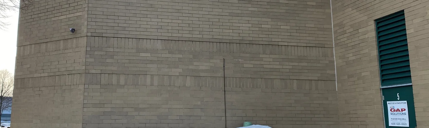 The corner of the Buffalo Grove building in 2021, buff brick with soldier course bands running around the corner and snow banked at the base