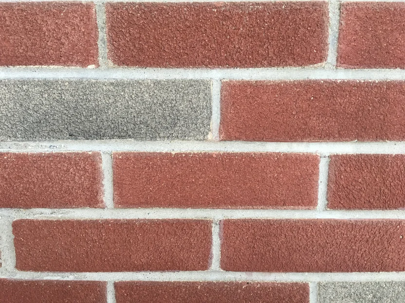 Brick at close range in 2019, red units with a sanded face in grey mortar joints, one grey unit in the second course