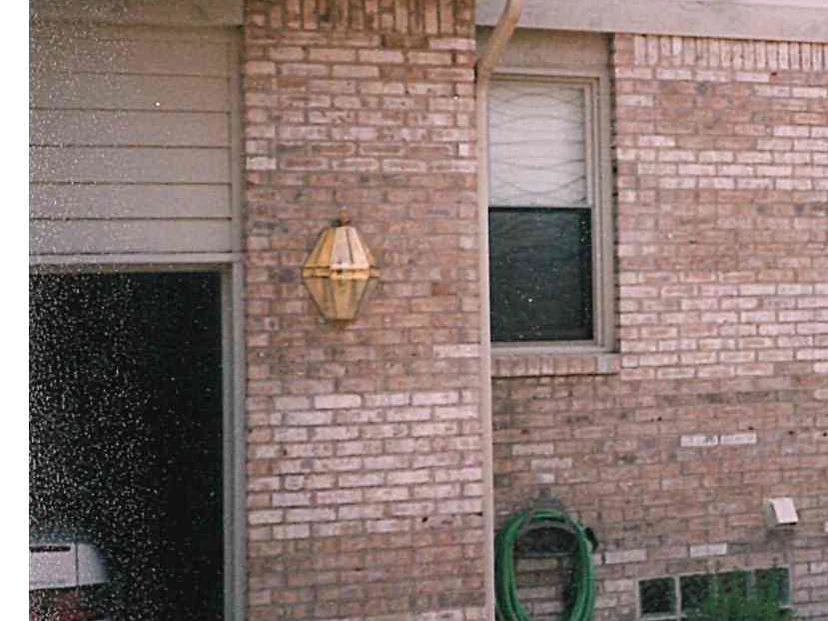 The brick pier between the garage and a window in 1997, a brass lantern on it and a coiled hose below, the units around the window a pale patch against darker ones