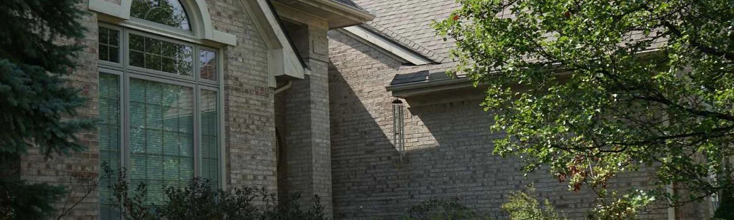 The front gable of the Canton house in 2019, an arched window set in cream and tan brick with a spruce and a shade tree either side