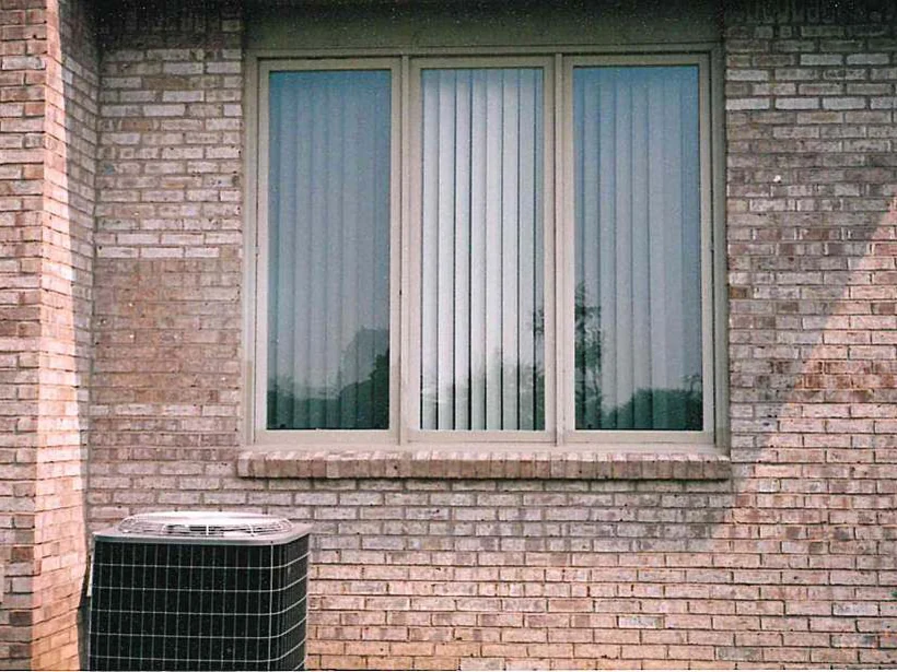 A three-pane window over an air conditioning unit in 1997, the brick around it mottled with a wide pale patch to the right of the frame
