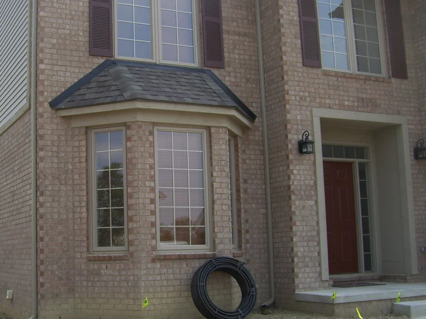 The front of the house in July 2010, a two-story bay window beside the entrance, orange header bricks standing out at every corner and around the bay against the pale face brick, bare dirt where the lawn will go