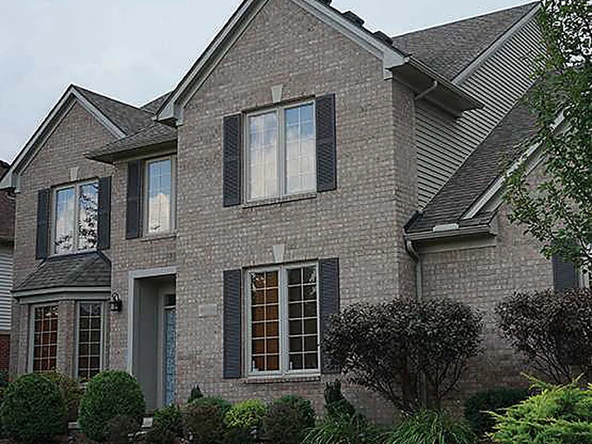 The front of the house in 2020, cream and tan brick reading as one blend across the gable, the bay window and the entrance, with grown shrubs along the bed and a shade tree at the corner
