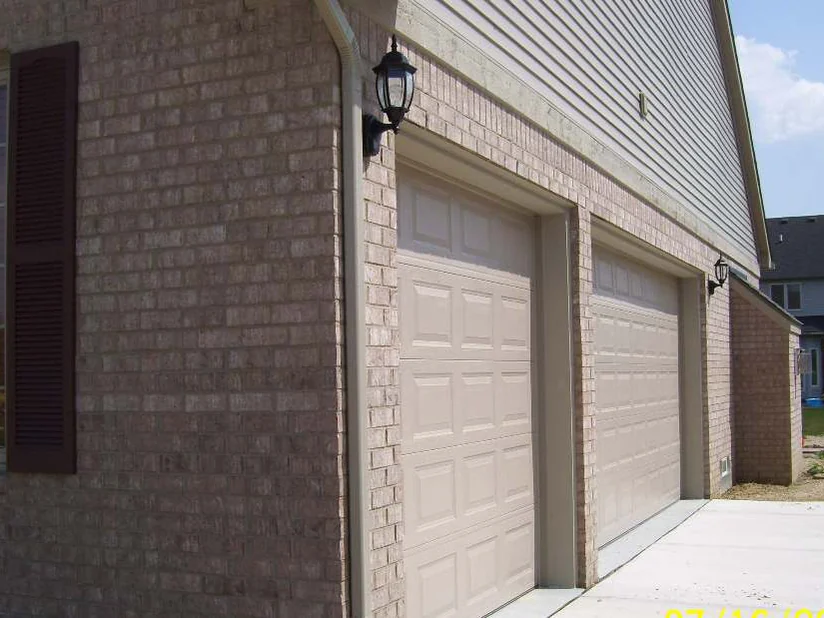 The same garage wall a day later, the framing courses and the corner pier matched to the field brick, a shuttered window at the left