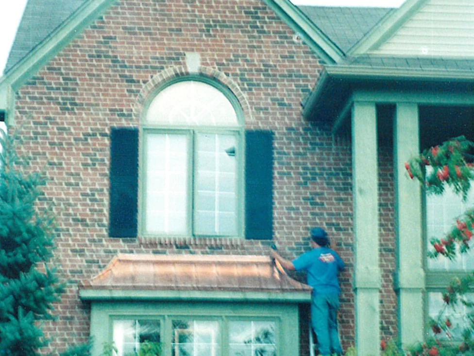 An applicator on a ladder in 1998, working the brick between the arched window and the porch by hand