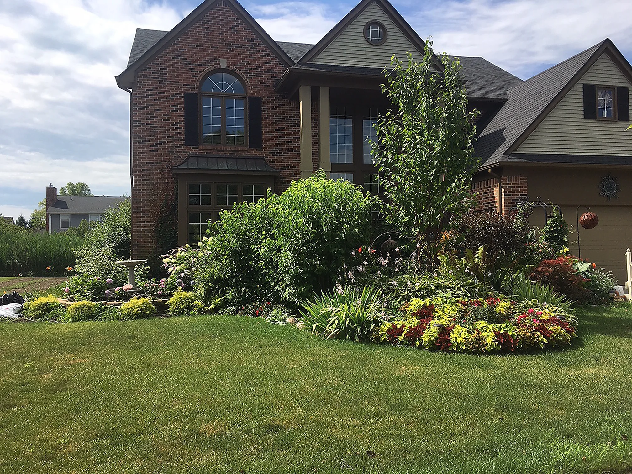 The front of the home from across the lawn in 2019, its brick one red and brown range behind deep planted beds and a young tree