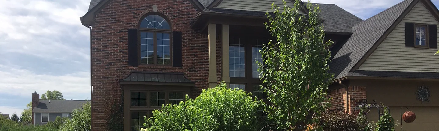The front of a two-story brick home in Canton, Michigan in 2019, its brick one red and brown range above deep garden beds