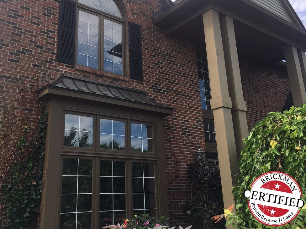 The same gable in 2019, the arched window and the bay below it set in one continuous red and brown range of brick, with a certification stamp in the corner