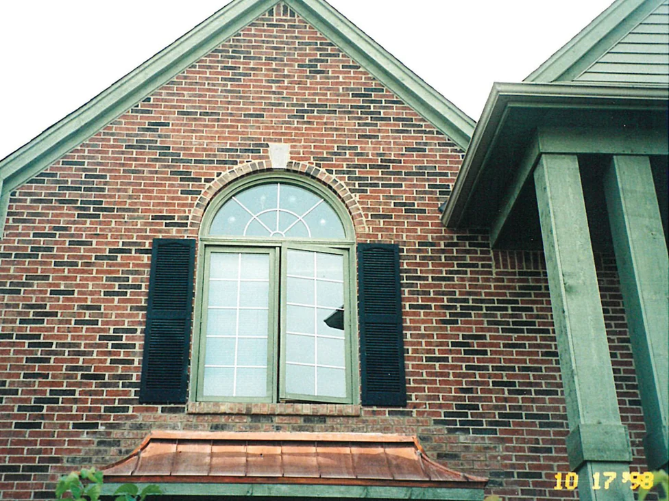 The gable end of the home in 1998, an arched window over a bay window with a copper roof, the brick a red and brown range with dark headers scattered through it