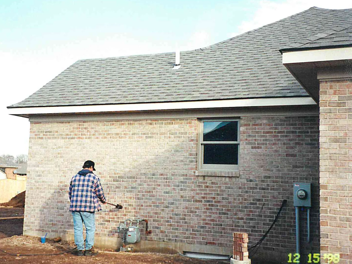 An applicator working stain across the side elevation of the house in 1998, the run of brick beside him already lighter than the wall beyond