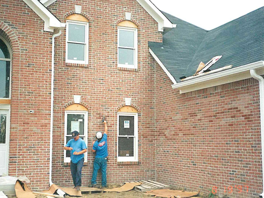 Two applicators working the brick of the house in 1997 while it was still under construction, the wall running an uneven red and tan