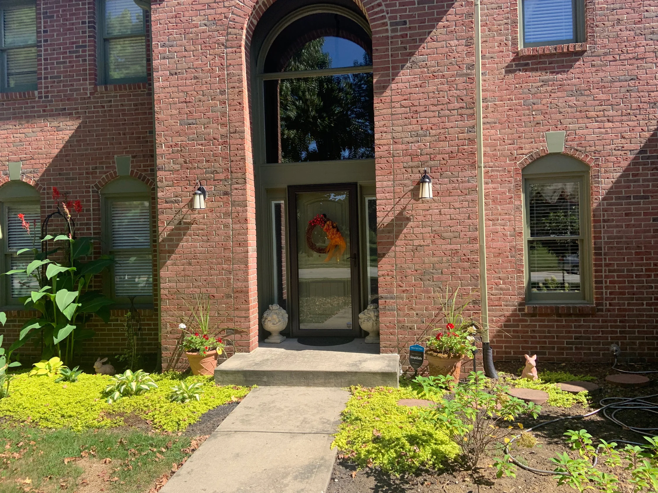 The arched front entry of the house in 2019, the brick running one even red and brown range from the beds up to the gable