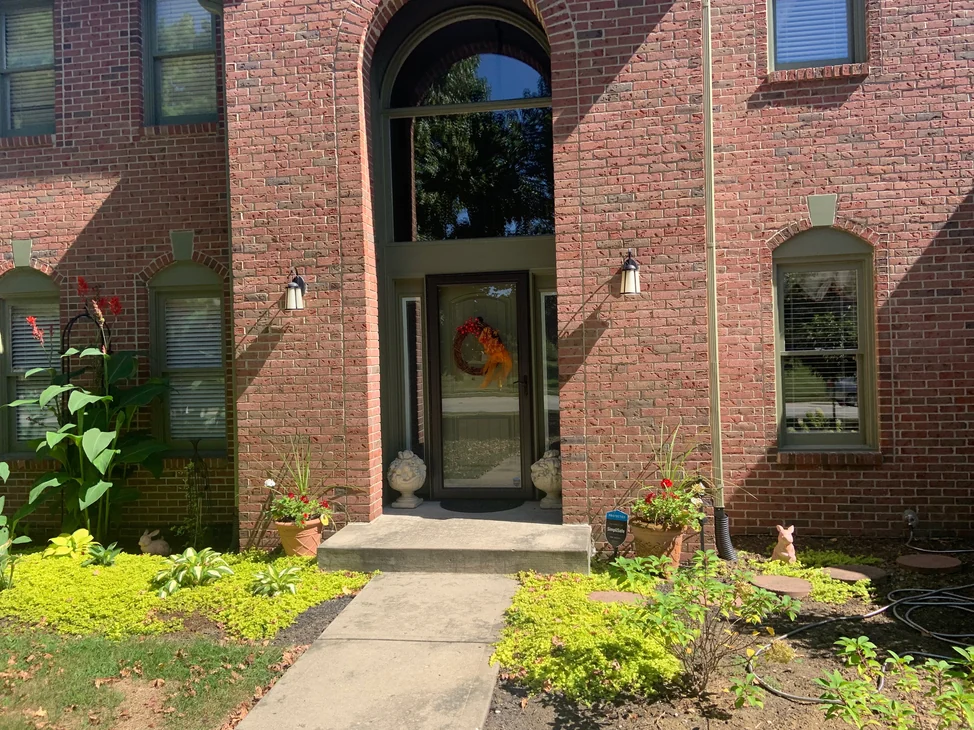 The arched front entry of the house in 2019, the brick running one even red and brown range from the beds up to the gable.
