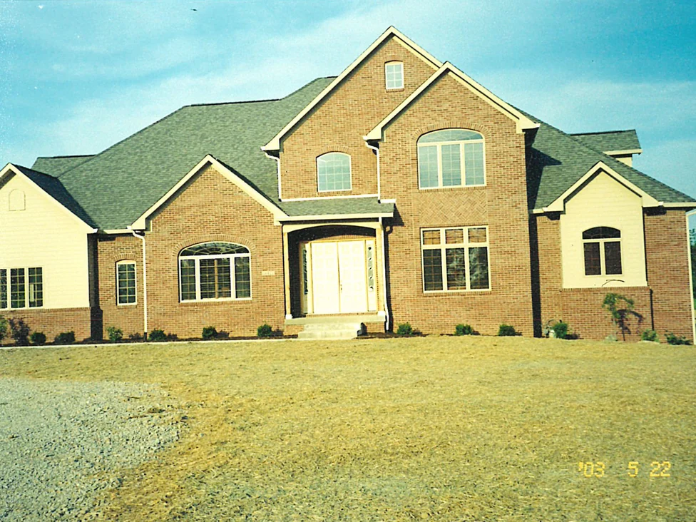 The whole front of the house in 2003 on a newly graded lot, the brick reading as one warm range across both wings and the entry