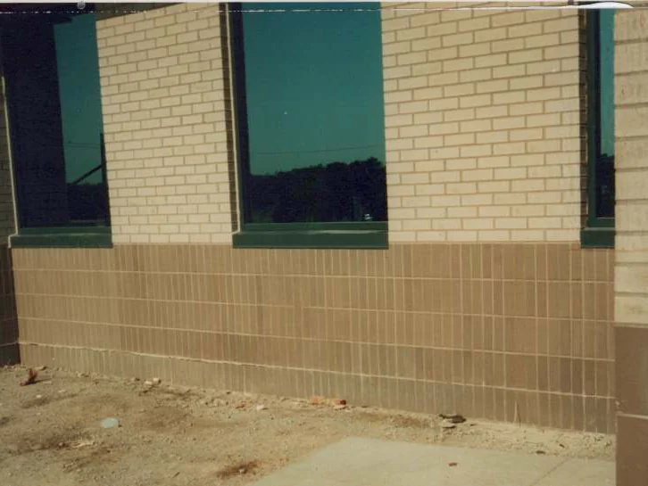 A corner of the building in 1995, tan base brick under cream brick and tinted windows, a pier at the right and bare ground in front