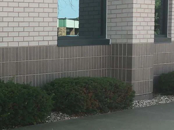 A window bay and pier in 2019, the base course one dark range under the cream brick, with yews along the sidewalk
