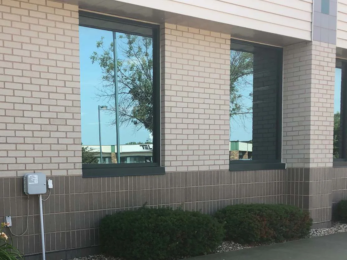 Three window bays of the Cedar Rapids office building in 2019, cream brick above a dark grey brown base course with yews planted along the foot of the wall