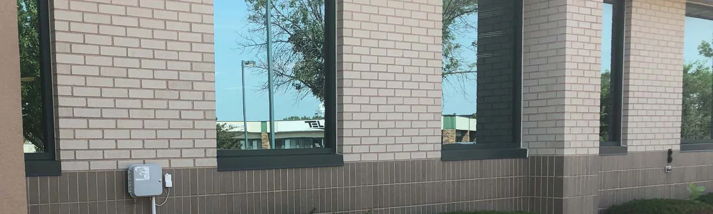 Three window bays of the Cedar Rapids office building in 2019, cream brick above a dark grey brown base course with yews planted along the foot of the wall