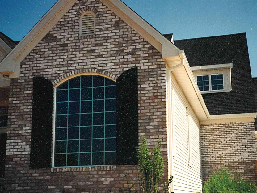 The gable end of the front wing in 1997, a large arched window between black shutters, dark brick scattered through the buff and tan units