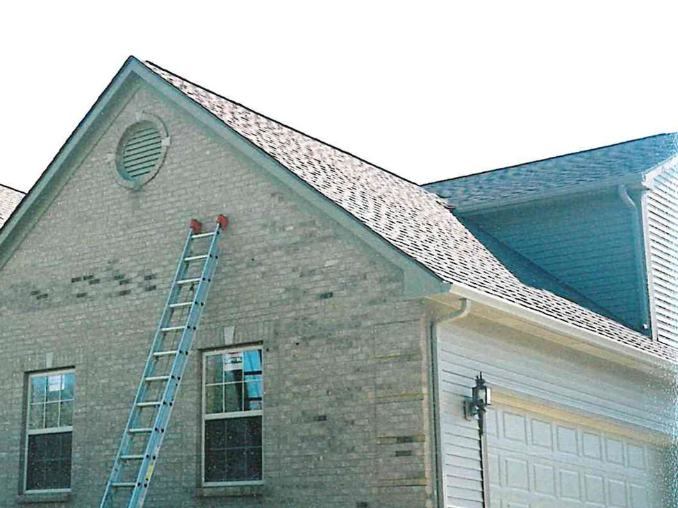 The gable end of the house in 2002 with an extension ladder leaning against it, a scattered band of dark bricks running across the pale wall below the round louvred vent