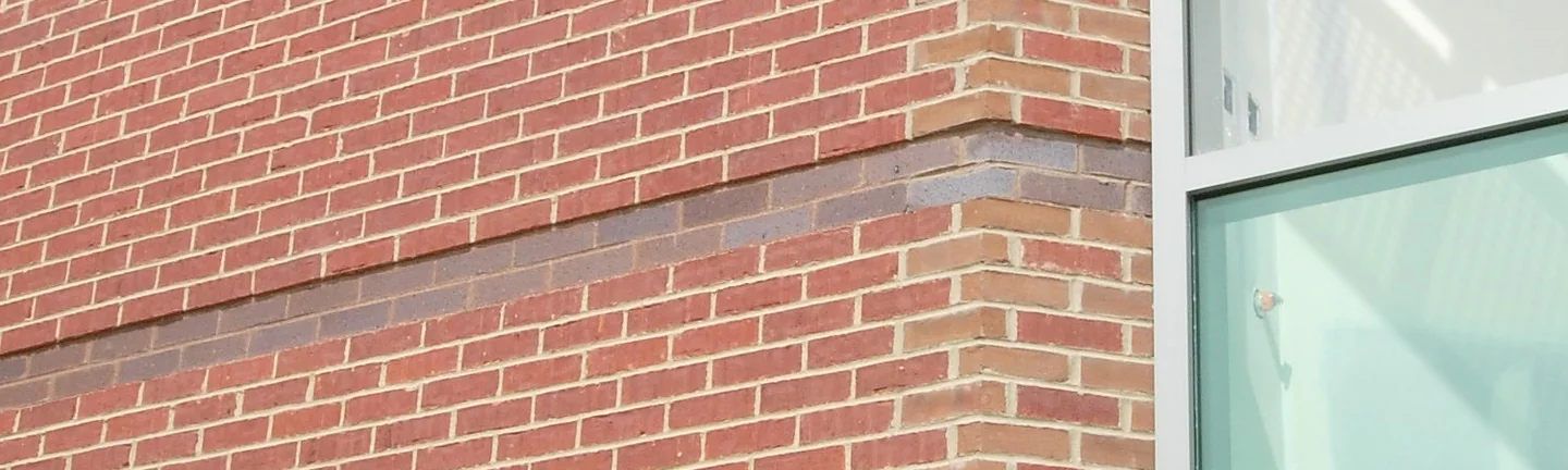 The 135 degree corner of the bank in 2004 before staining, red brick with two dark accent courses and the corner units reading lighter than the wall, a window bay to the right