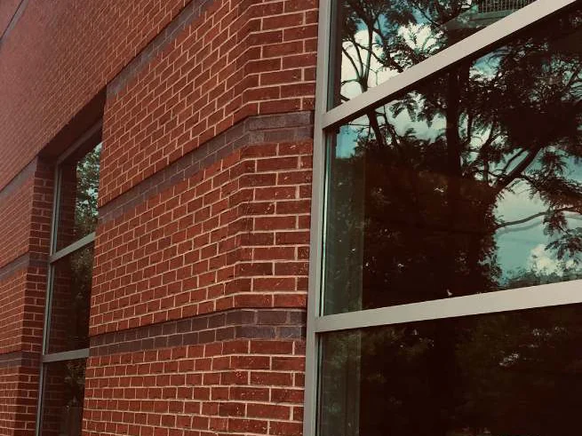 The corner of the bank in 2019 from further back, the stained corner shapes between two dark accent courses with a window bay on each side reflecting trees