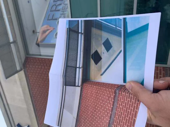 A hand holding a printed 2004 photograph of the corner up in front of the brick in 2021, a window poster behind it