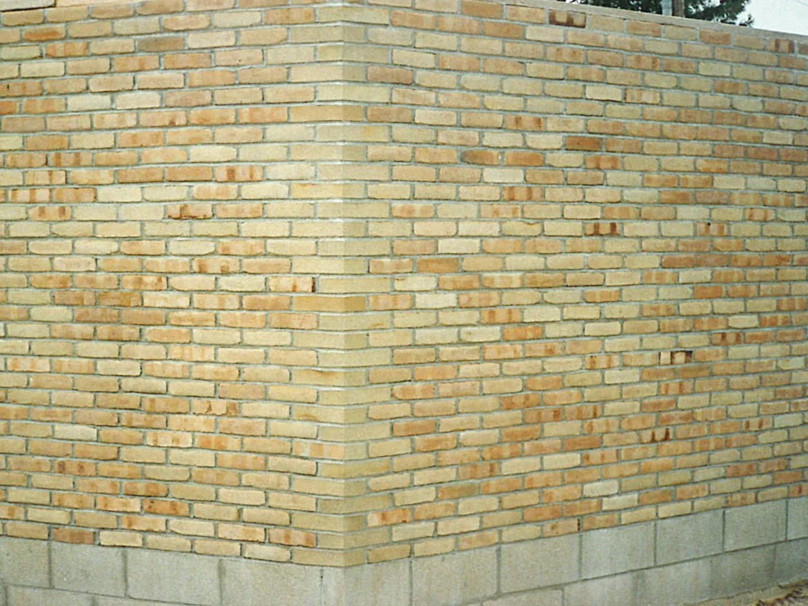 The outside corner of a buff brick wall on a block base in 1996, the corner units reading as one flat pale tan against the mottled stretchers on both faces
