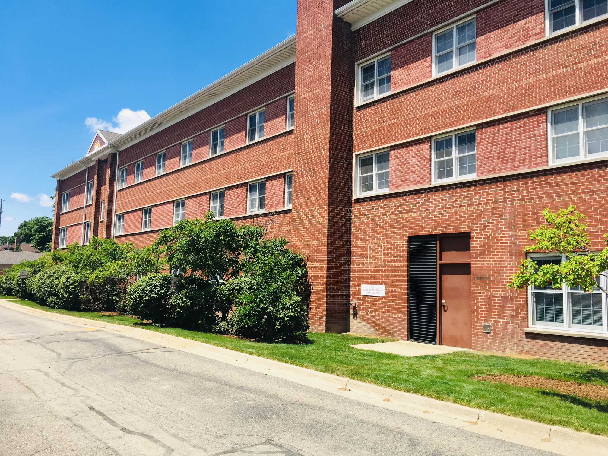 The three-story elevation running away down the service drive in 2019, red brick with the window bands a lighter red the whole length of the wall