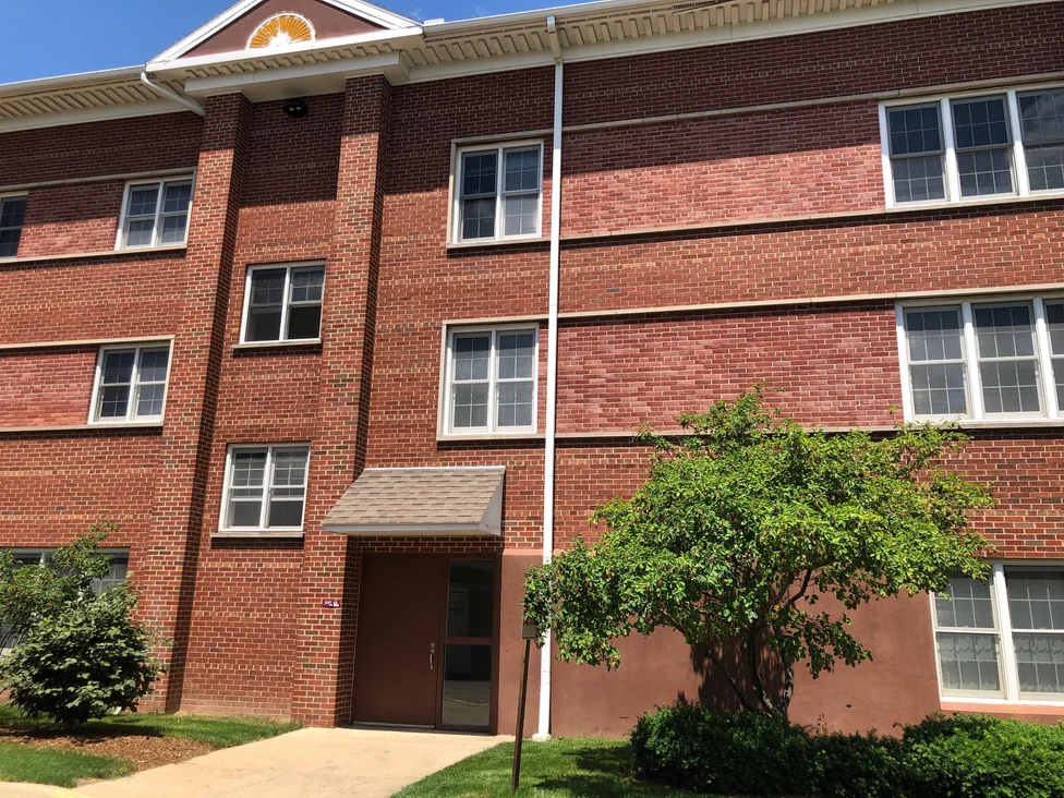 A side entrance under a shingled hood in 2019, with the pediment and its carved sunburst above and red brick on every course