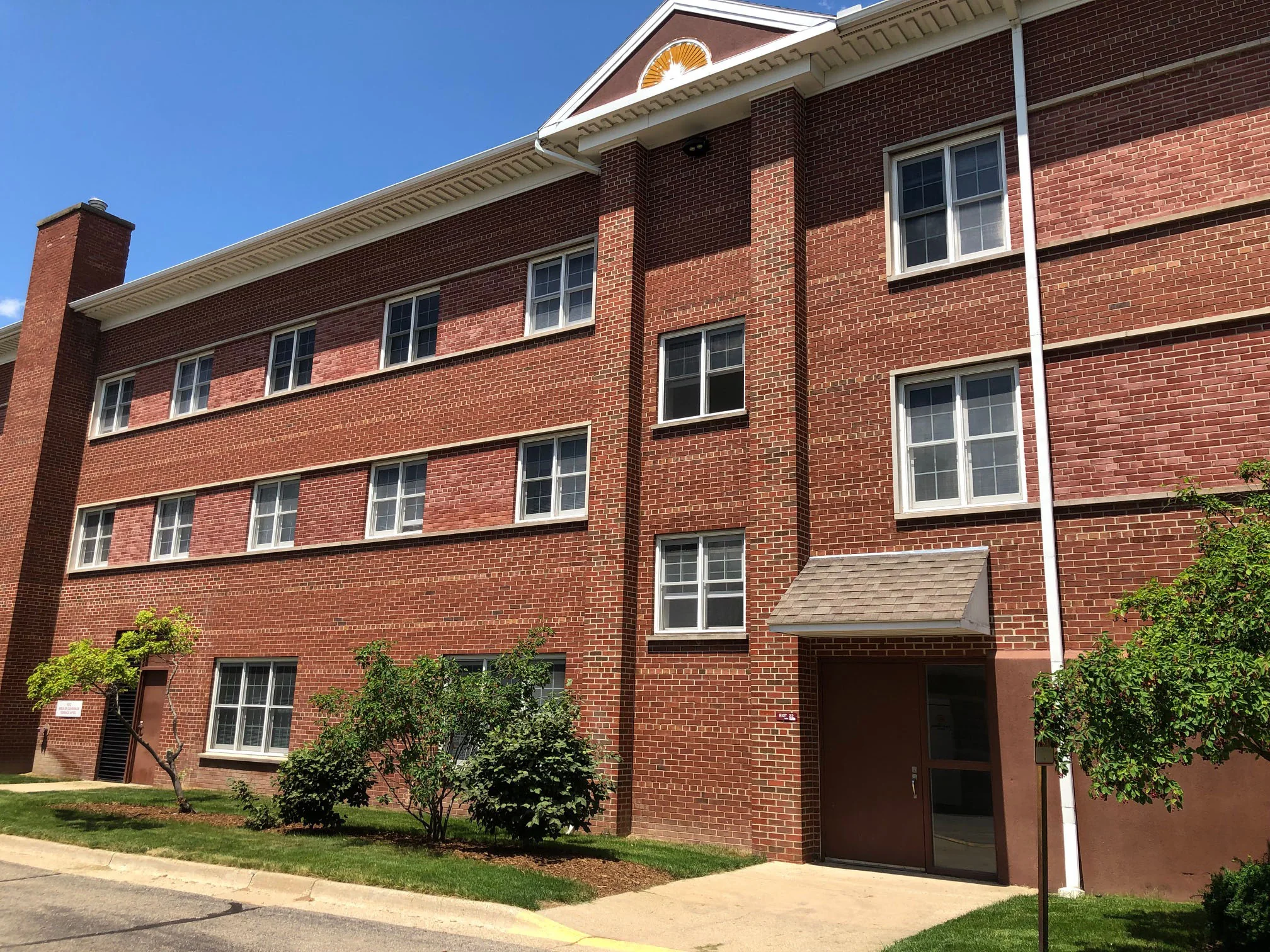 The gabled end of the building in 2019, red brick from the ground to the pediment, with the two window bands reading a lighter red than the courses around them