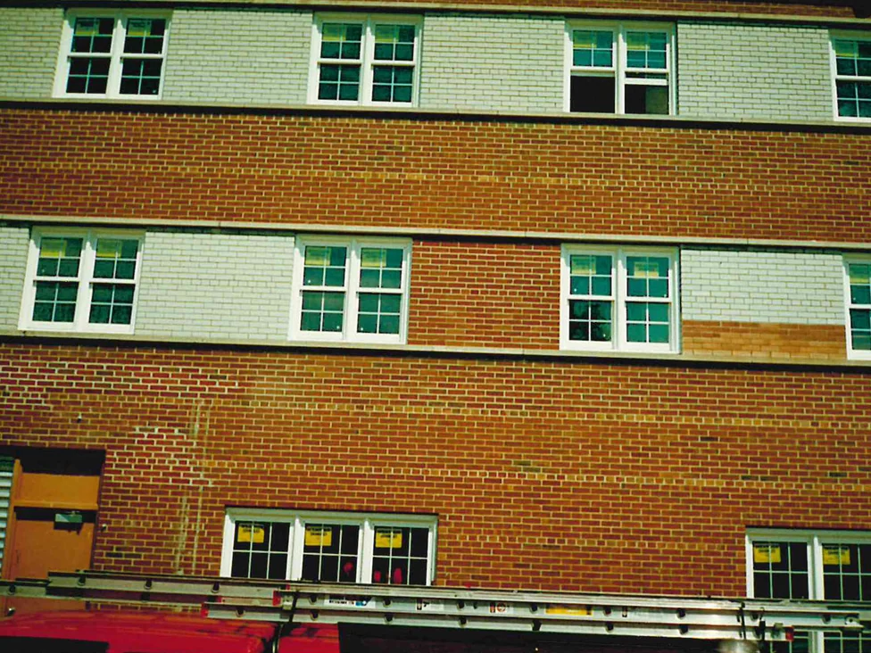 One window band caught part way through the work: white brick to the right of the windows, a course of pale tan below it, and red brick to the left, with an extension ladder on a van roof rack across the foot of the frame