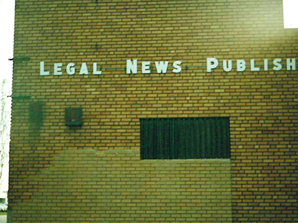 A buff brick office wall in 1996 with a lettered sign band across it, a large rectangle of replacement brick standing out paler than the brick around it