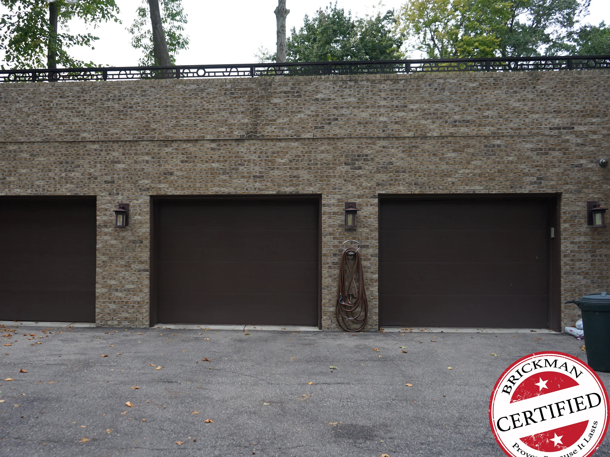 The garage wing square on in 2019, its brick one warm tan and brown blend across all three bays, under a run of iron railing at the parapet