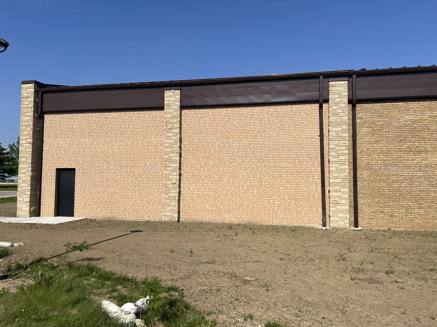 A commercial building where a new run of pink-toned brick meets the tan brick of the older wall at a stone pier