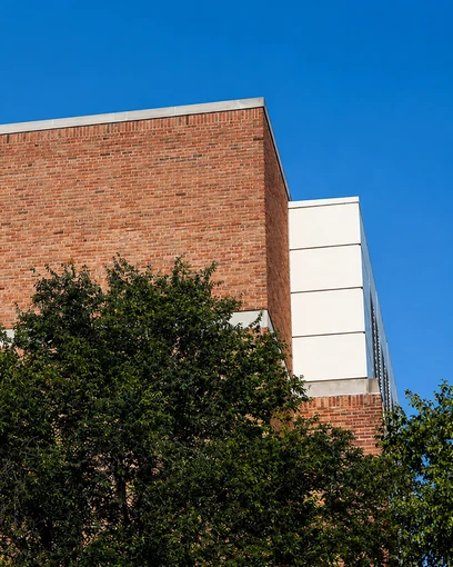 Upward view of the corner of a brick building, its courses banded with cream precast panels, against a clear blue sky