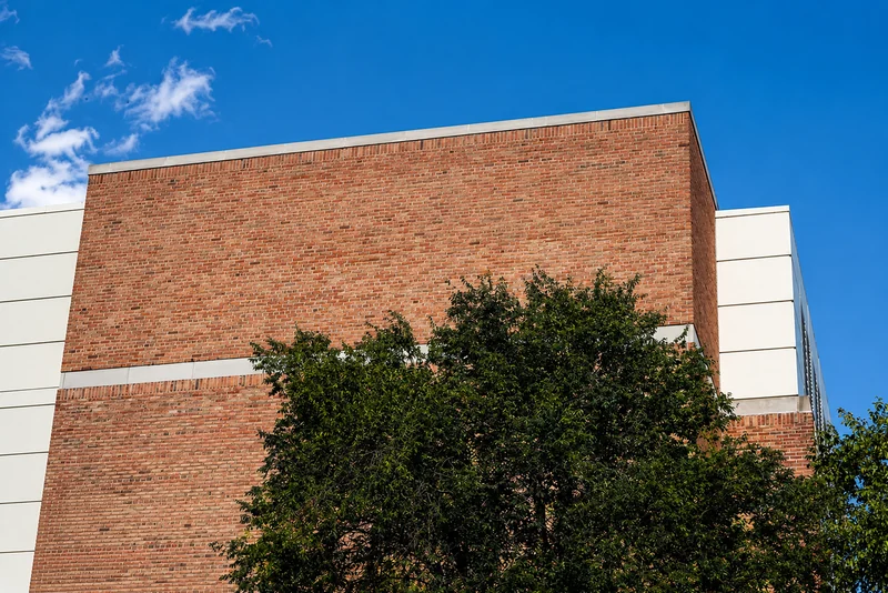 Upward view of the corner of a brick building, its courses banded with cream precast panels, against a clear blue sky