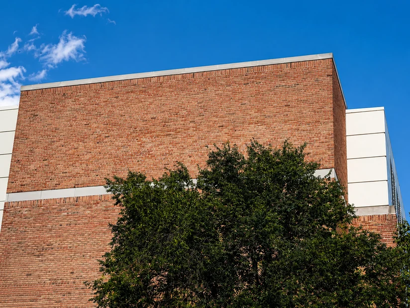Upward view of the corner of a brick building, its courses banded with cream precast panels, against a clear blue sky