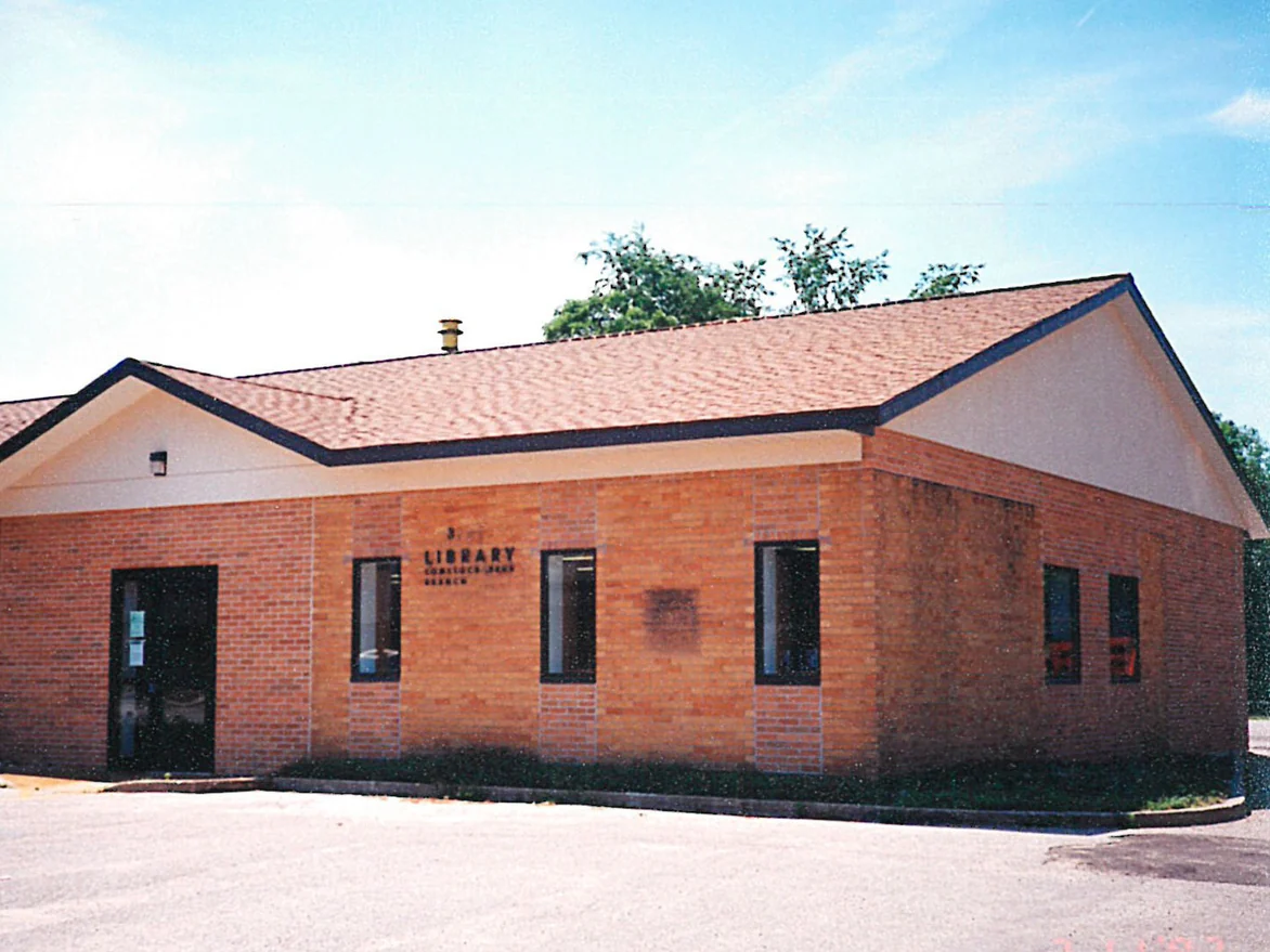 The branch library from its parking lot in 1997, the orange brick front interrupted by taller panels of a pinker, greyer brick between the windows and by one dark rectangular patch
