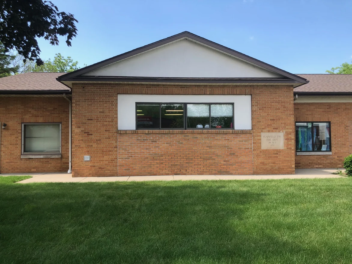 The gable end of the library square on in 2019, a ribbon window over plain brick with a carved 1952 fire department cornerstone set into the wall at the right