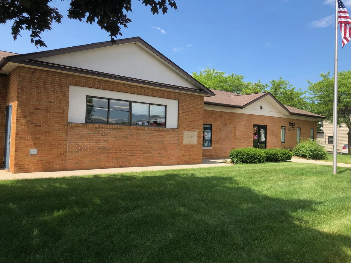The library in 2019 from the lawn beside the flagpole, the gable end, the stone cornerstone and the entrance all in one continuous run of brick