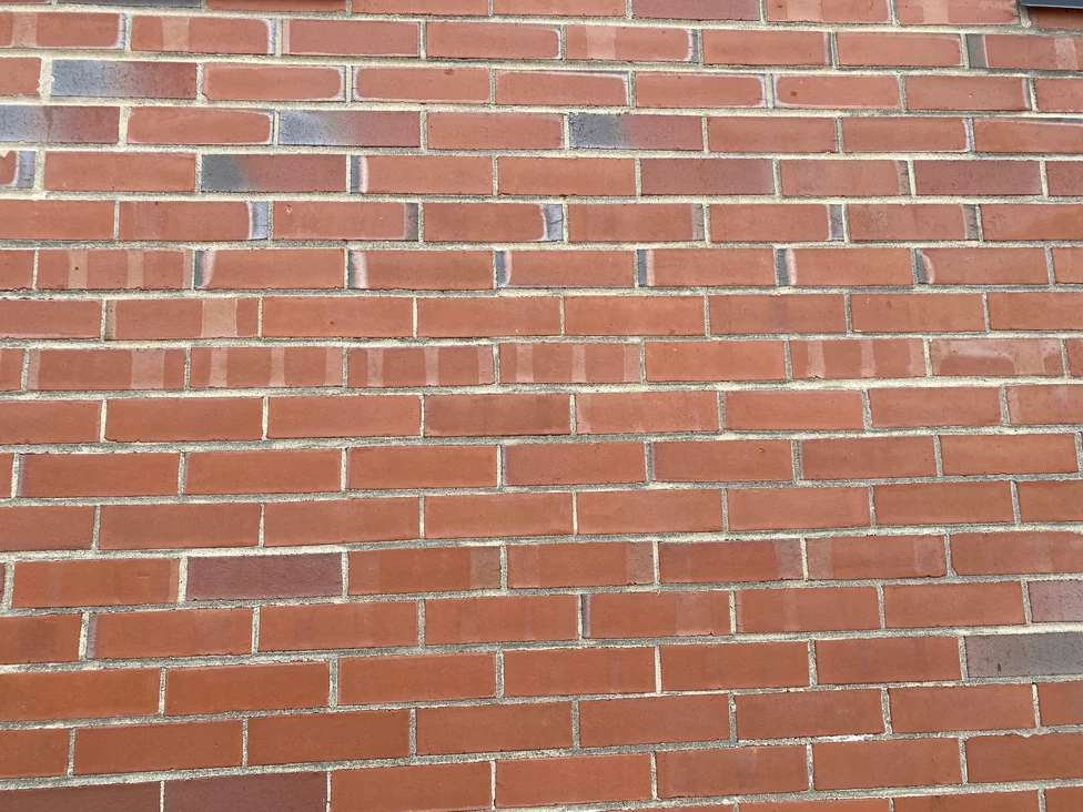 The wall at unit scale in 2021, red brick in running bond with scattered darker headers, a few faces reading slightly different in tone from the units around them