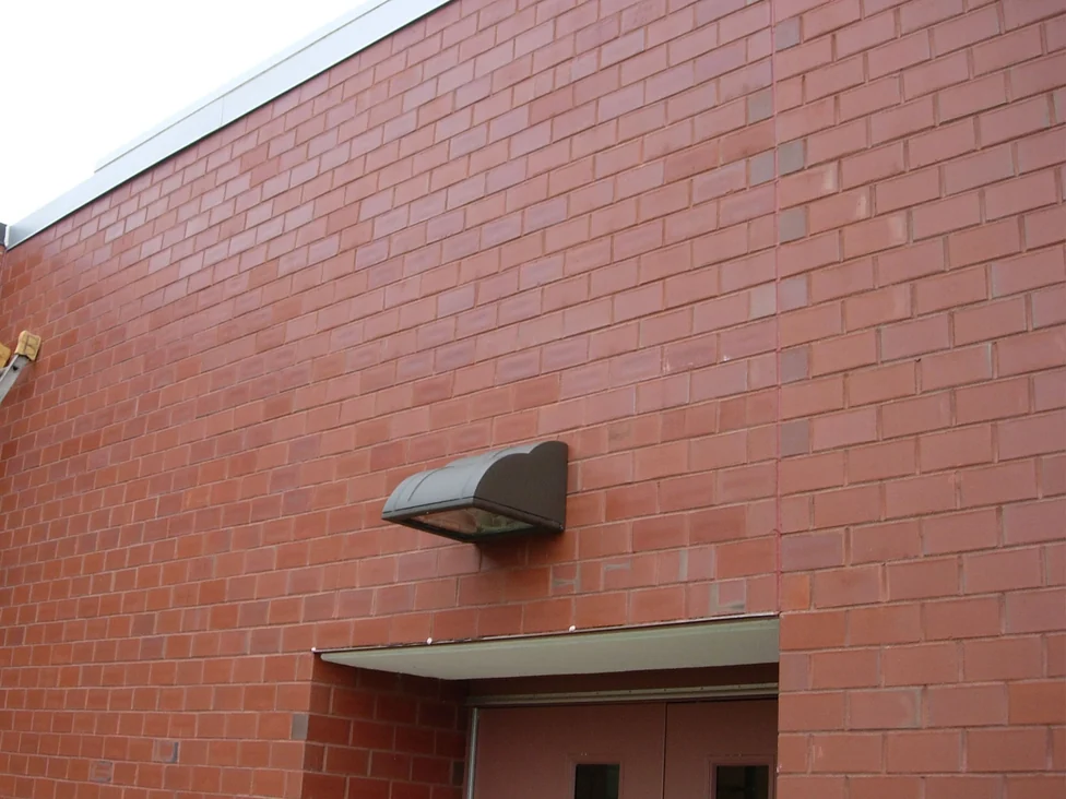 The same red brick wall above the school entrance in 2007 after staining, the white blotches blended into the surrounding units, with the wall light and the top of the ladder at the left edge